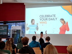 A seminar room with attendees focused on a presentation slide encouraging the celebration of daily wins. The room features banners for Max Planck School Matter to Life and DWI, Leibniz Institute for Interactive Materials.
