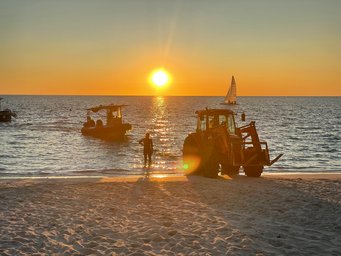After sample collection, the research vessel is pulled back ashore with a tractor Sunset on the sea in Australia with boat in the water and tractor on the beach