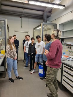 A group of students stand in a lab during a tour by doctoral student Michele Stasi.