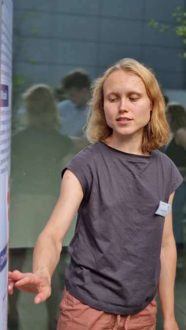 Alena Taskina shows something on her poster with her right hand. In the reflection of the glazed background you can see several people standing around her.