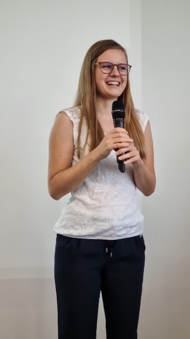 Kathrin Laxhuber holds the microphone with both hands and gives the audience a warm, broad smile as she gives a brief outline of the topic of her poster.