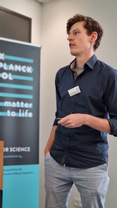 Benedikt Rennekamp changes the slide with the laser pointer, his right hand casually in his pocket, the MPS MtL roll-up to his left.
