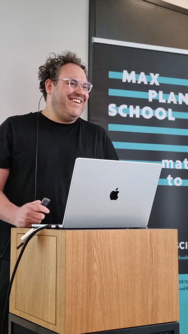 Guest speaker Julian Grünewald stands at the lectern and laughs heartily into the audience.