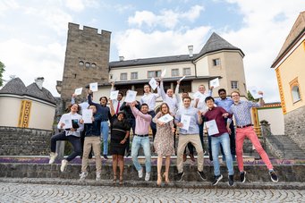 Congratulations to our second cohort! Another picture from the inner courtyard, in the middle of the same scenery: Around 20 students hold their certificates in their hands and jump up, cheering.