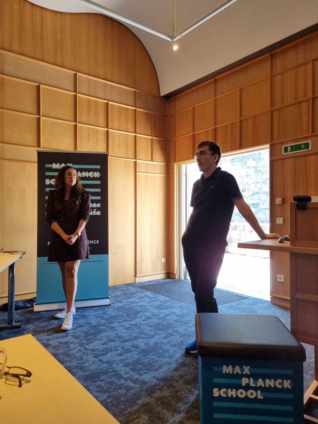 Two MtL students are standing at the front, a moderator, Brianda Lopez Santini, and Douglas Diel who is giving the presentation, who is answering questions while leaning on the lectern.