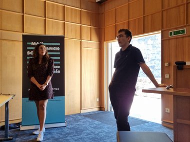 Two MtL students are standing at the front, a moderator, Brianda Lopez Santini, and Douglas Diel who is giving the presentation, who is answering questions while leaning on the lectern.