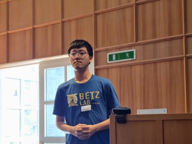 An MtL student stands with his hands clasped next to the lectern. He is wearing a shirt with the inscription "Betz Lab", the laboratory of faculty member Timo Betz.