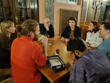 A group of participant is sitting around a wodden table and setting up a board game