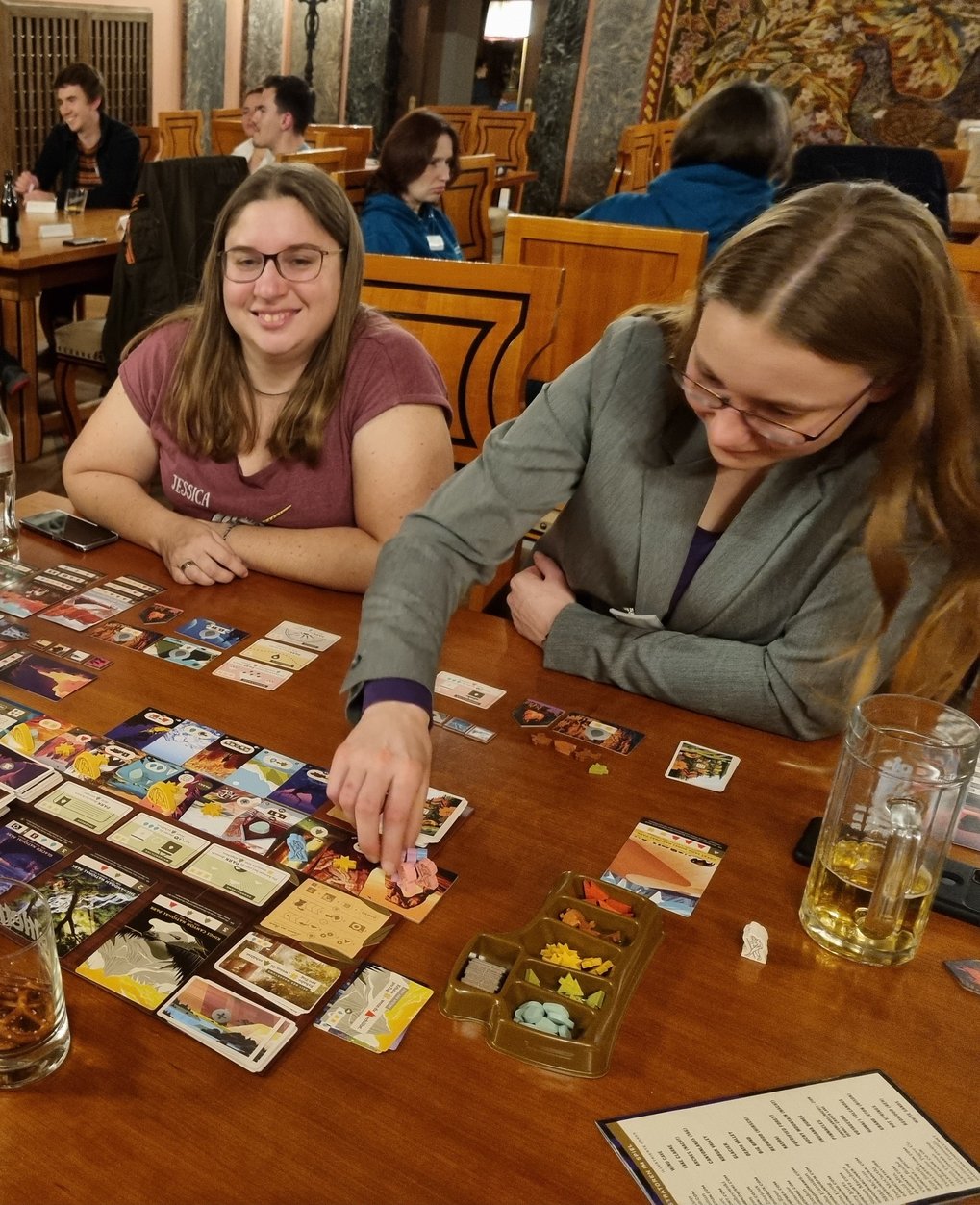 Two female participants sit at a wooden table and play a board game