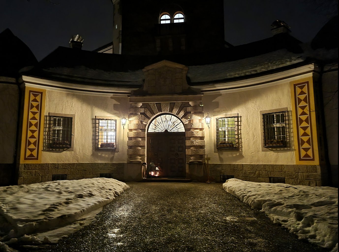 Path to the illuminated entrance of Ringberg Castle in the evening, there is snow next to the path