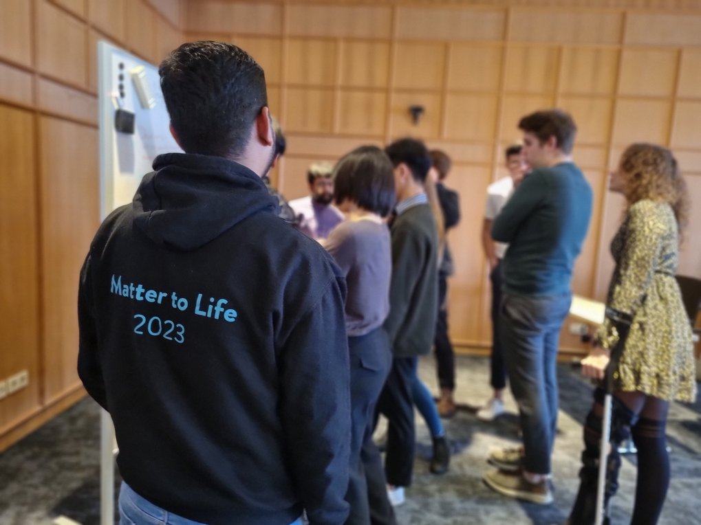 A group of students stand in front of a whiteboard. In the foreground you can see the inscription "Matter to Life 2023" on the back of the hoodie of a student
