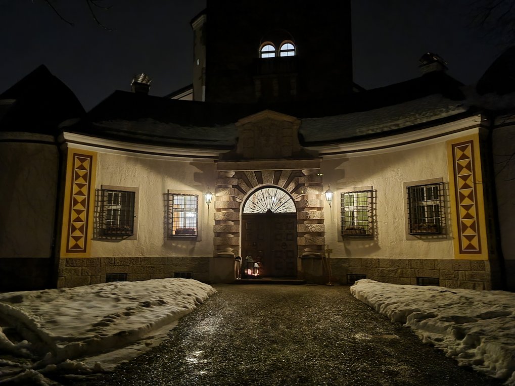 Path to the illuminated entrance of Ringberg Castle in the evening, there is snow next to the path