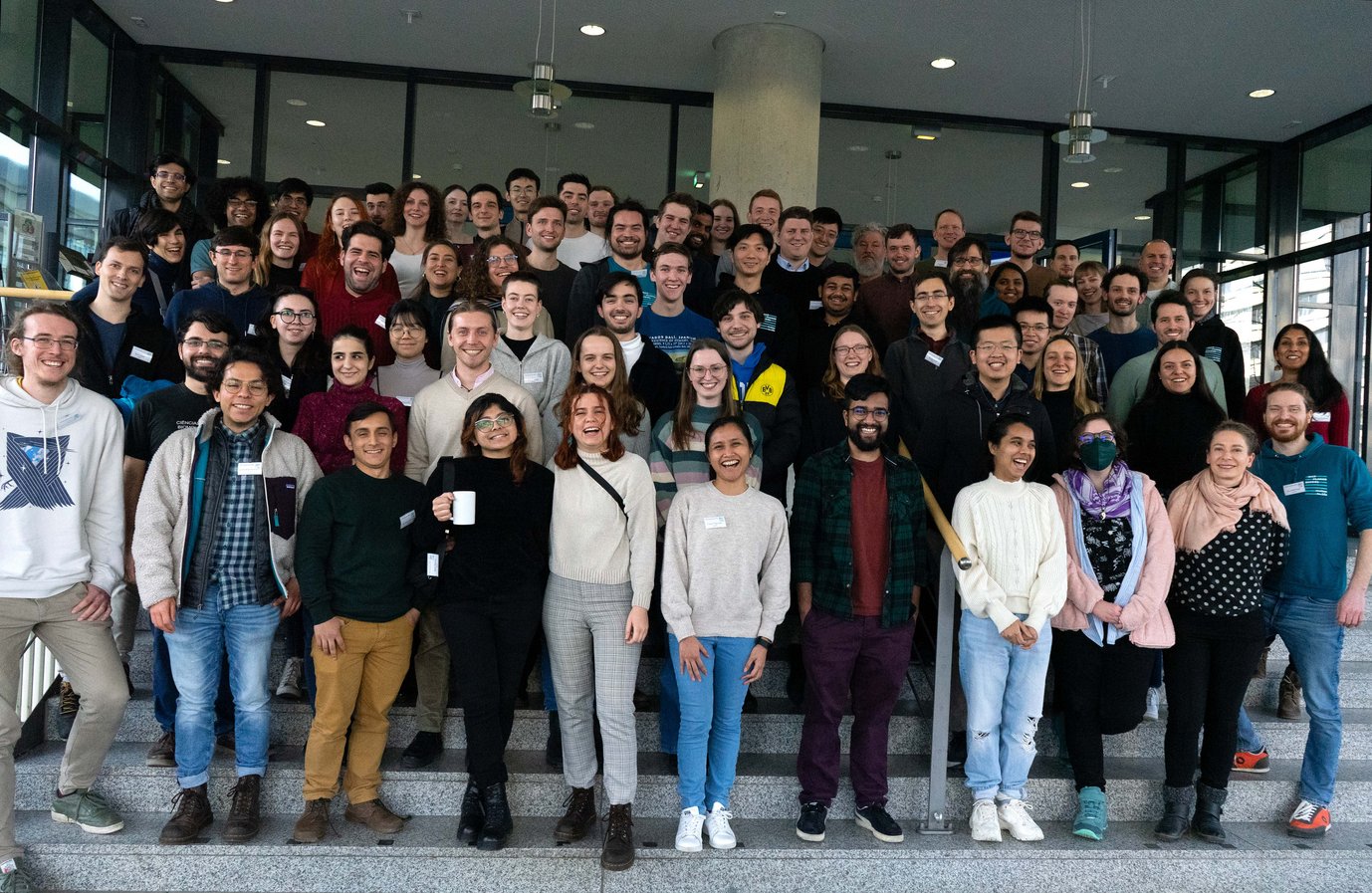 Matter to Life PhD candidates participating in the MtL Spring Days 2024 stand on the stairs at the main entrance of the physics building at the University of Göttingen 