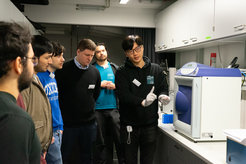 Matter to Life PhD students stand together in a science lab, one of the PhD students explains an application to the others