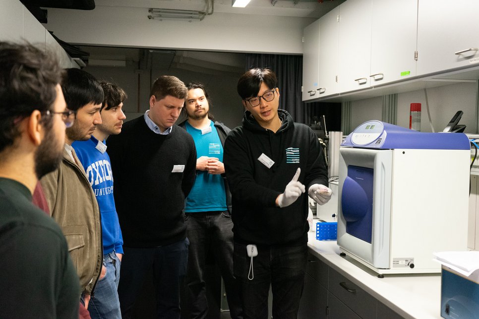Matter to Life PhD students stand together in a science lab, one of the PhD students explains an application to the others

