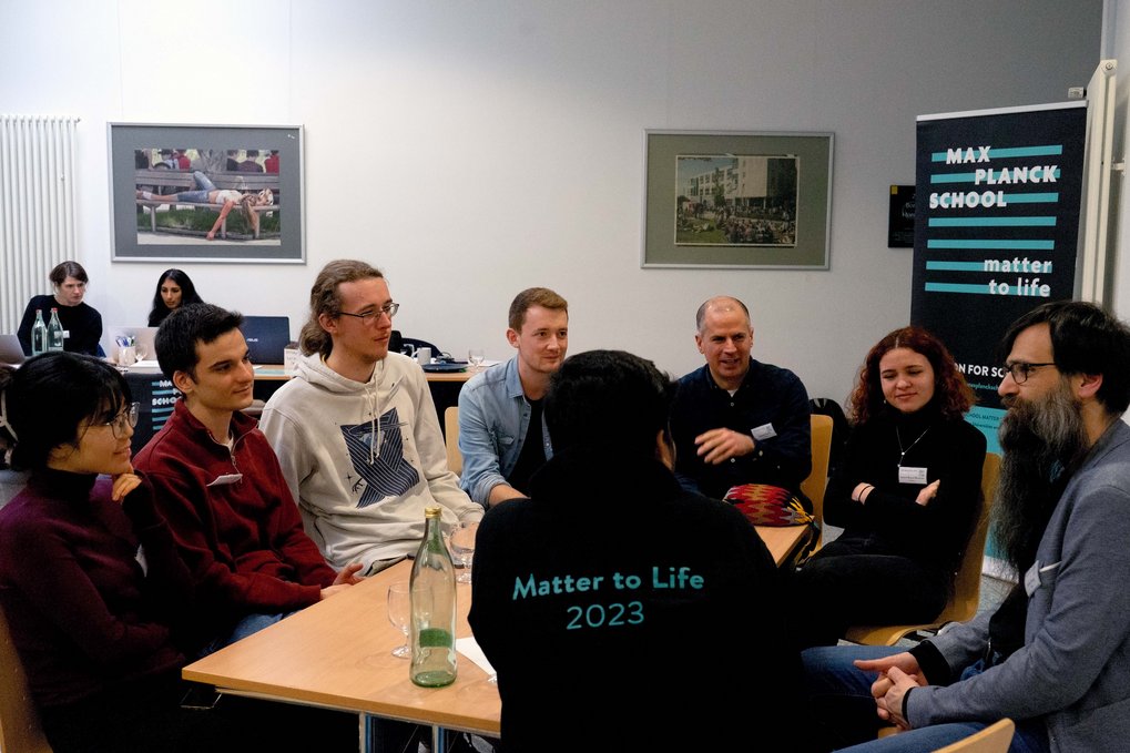 PhD candidates sit around a table with Matter to Life Fellow Stefan Klumpp and discuss