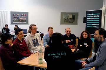 PhD candidates sit around a table with Matter to Life Fellow Stefan Klumpp and discuss