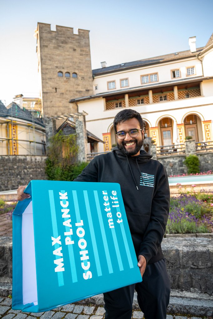 A student holds a seat cube on which the Matter to Life logo is displayed in large letters. Ringberg Castle can be seen in the background. 