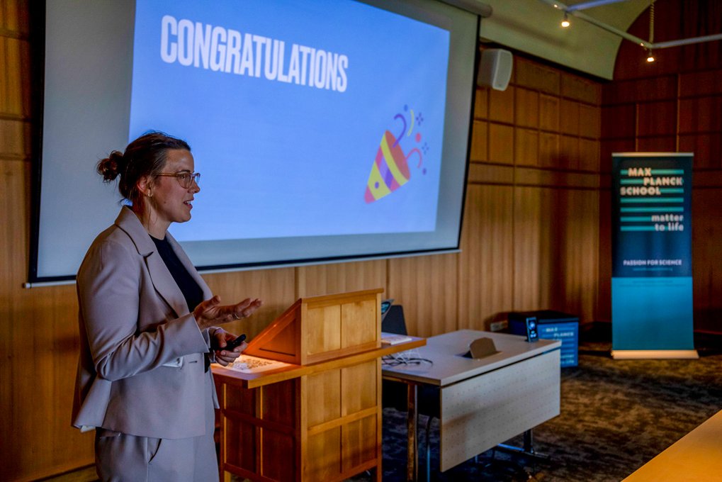 The group leader of the Max Planck Schools, Johanna Rapp, is giving a lecture. She is standing in front of a screen on which her presentation can be seen, with “Congratulations” written on it with a party hat. 