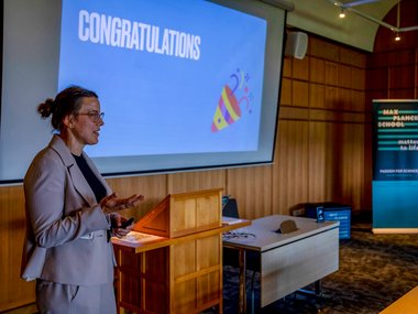 The group leader of the Max Planck Schools, Johanna Rapp, is giving a lecture. She is standing in front of a screen on which her presentation can be seen, with “Congratulations” written on it with a party hat.