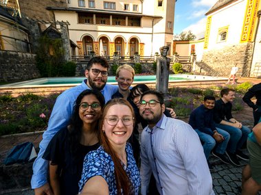 Three female and three male students take a selfie. The scenery of Ringberg Castle can be seen in the background