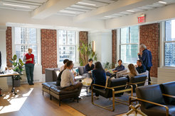 A group of Matter to Life conference participants converse in a bright lounge with brick walls, large windows, and modern furniture