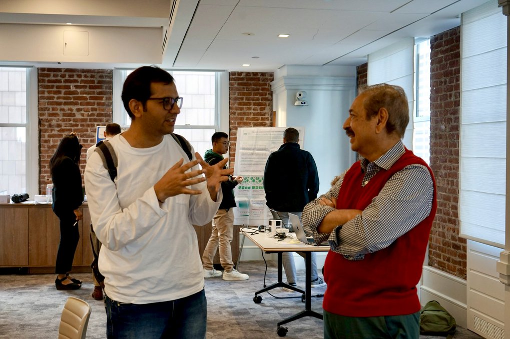 Two men discussing in a conference room, with a table and chairs visible in the background.