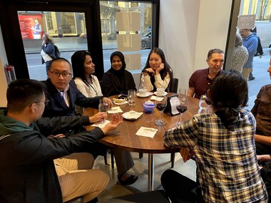 A group of participants at the Matter to Life conference are sitting at a table in a restaurant, chatting and drinking something.