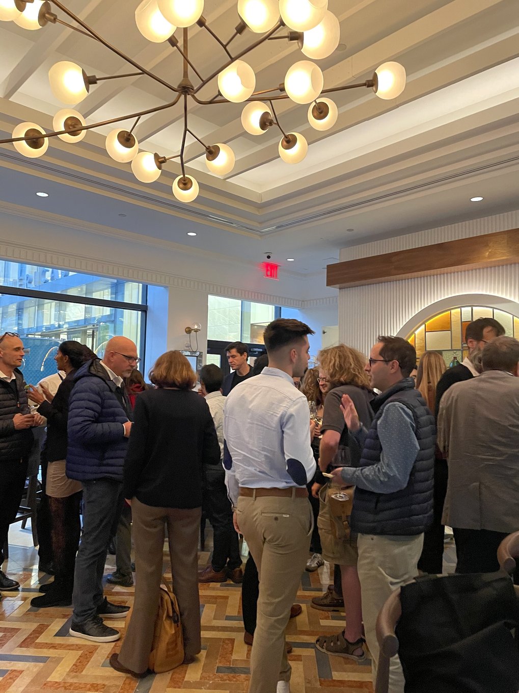 A group of conference attendees stands in a lobby adorned with chandeliers during a restaurant reception