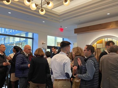 A group of conference attendees stands in a lobby adorned with chandeliers during a restaurant reception