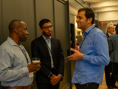 Three men engaged in conversation, one holding a coffee cup, creating a casual and collaborative atmosphere.