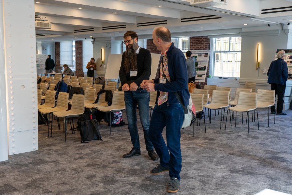 In a room with chairs and tables, Frank Jülicher and Stefan Klumpp share a conversation, smiling and laughing.