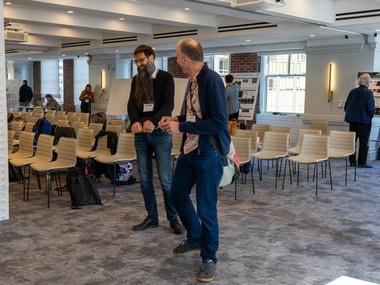 In a room with chairs and tables, Frank Jülicher and Stefan Klumpp share a conversation, smiling and laughing.