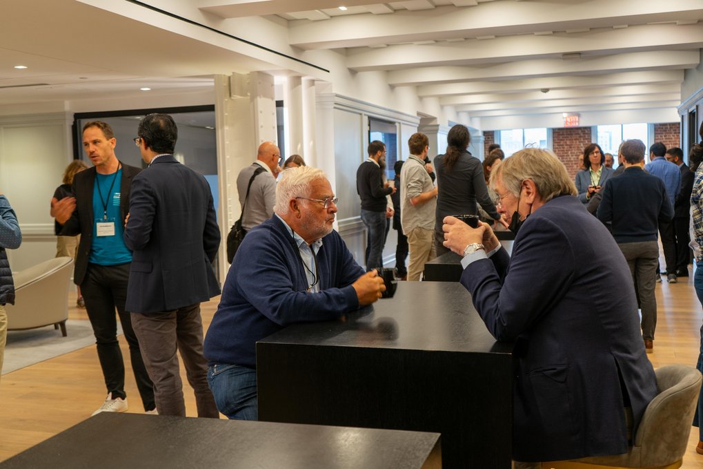A group of individuals engaged in discussion around tables in a well-lit conference room setting