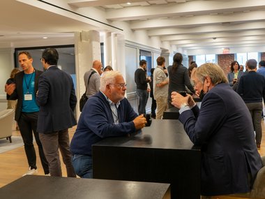 A group of individuals engaged in discussion around tables in a well-lit conference room setting