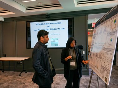Two persons looking at a scientific poster, the woman is explaining something to the man.
