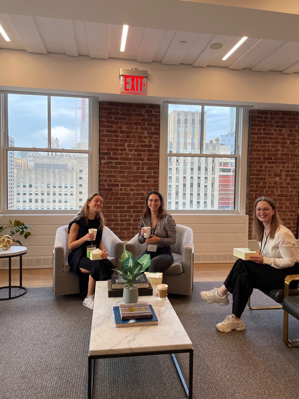 Three Matter to Life doctoral students sit in a cozy room with a view of the city in the background. Each holds a coffee cup and enjoys the company of the other.