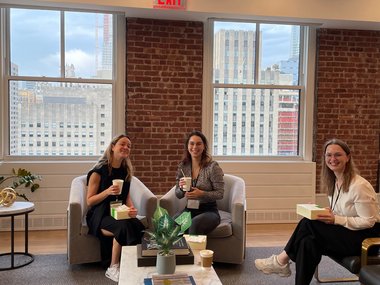 Three Matter to Life doctoral students sit in a cozy room with a view of the city in the background. Each holds a coffee cup and enjoys the company of the other.