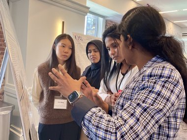 4 women standing in front of a scientific poster and discussing