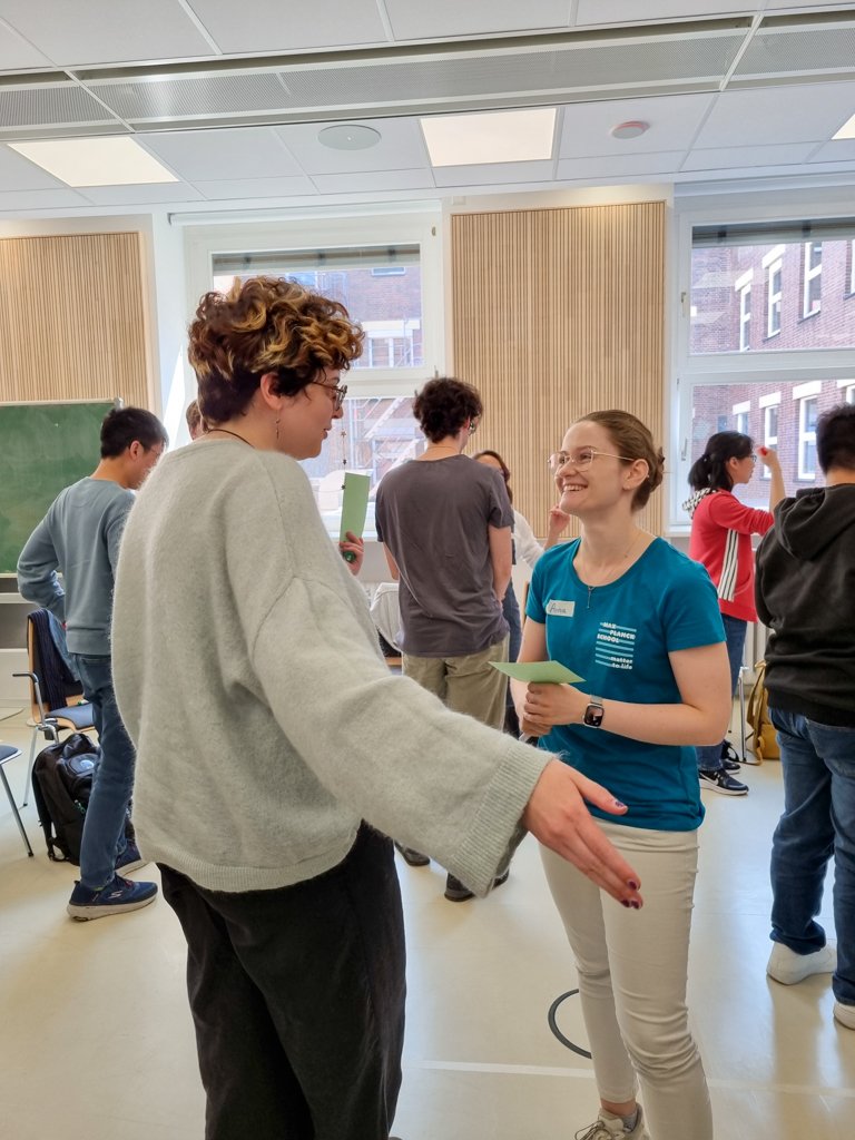 Two people engaged in a lively conversation during a group activity in a bright meeting room, with others interacting in the background