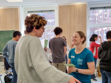 Two people engaged in a lively conversation during a group activity in a bright meeting room, with others interacting in the background