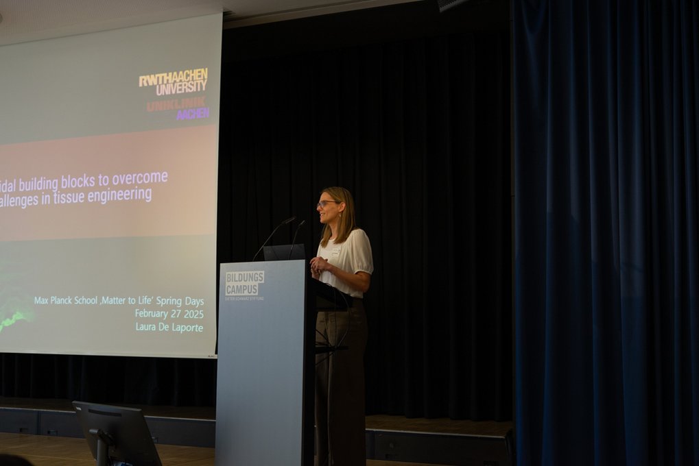A conference presentation addresses overcoming challenges in tissue engineering, featuring speaker Laura De Laporte at the Max Planck School event.