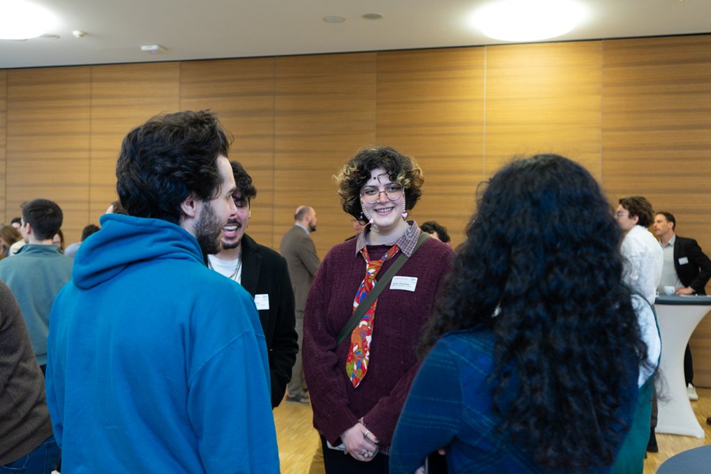 Group of people in a room with wooden wall panels, engaging in conversation.