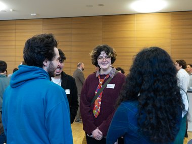 Group of people in a room with wooden wall panels, engaging in conversation.