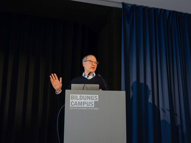Ulrich Schwarz at podium with "Bildungscampus" logo, hand raised in gesture.