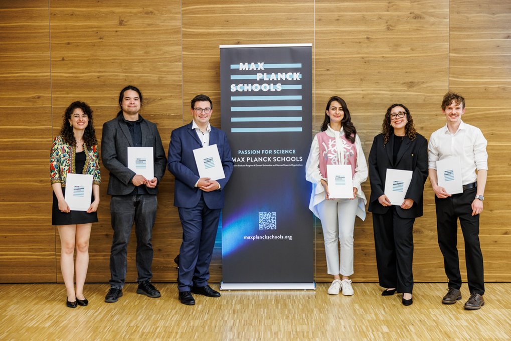 Seven graduates of the Max Planck Schools standing with their certificates in front of a Max Planck Schools banner – celebrating the successful completion of a scientific program