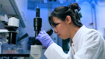 A scientist in a lab coat looks through a microscope in a lab
