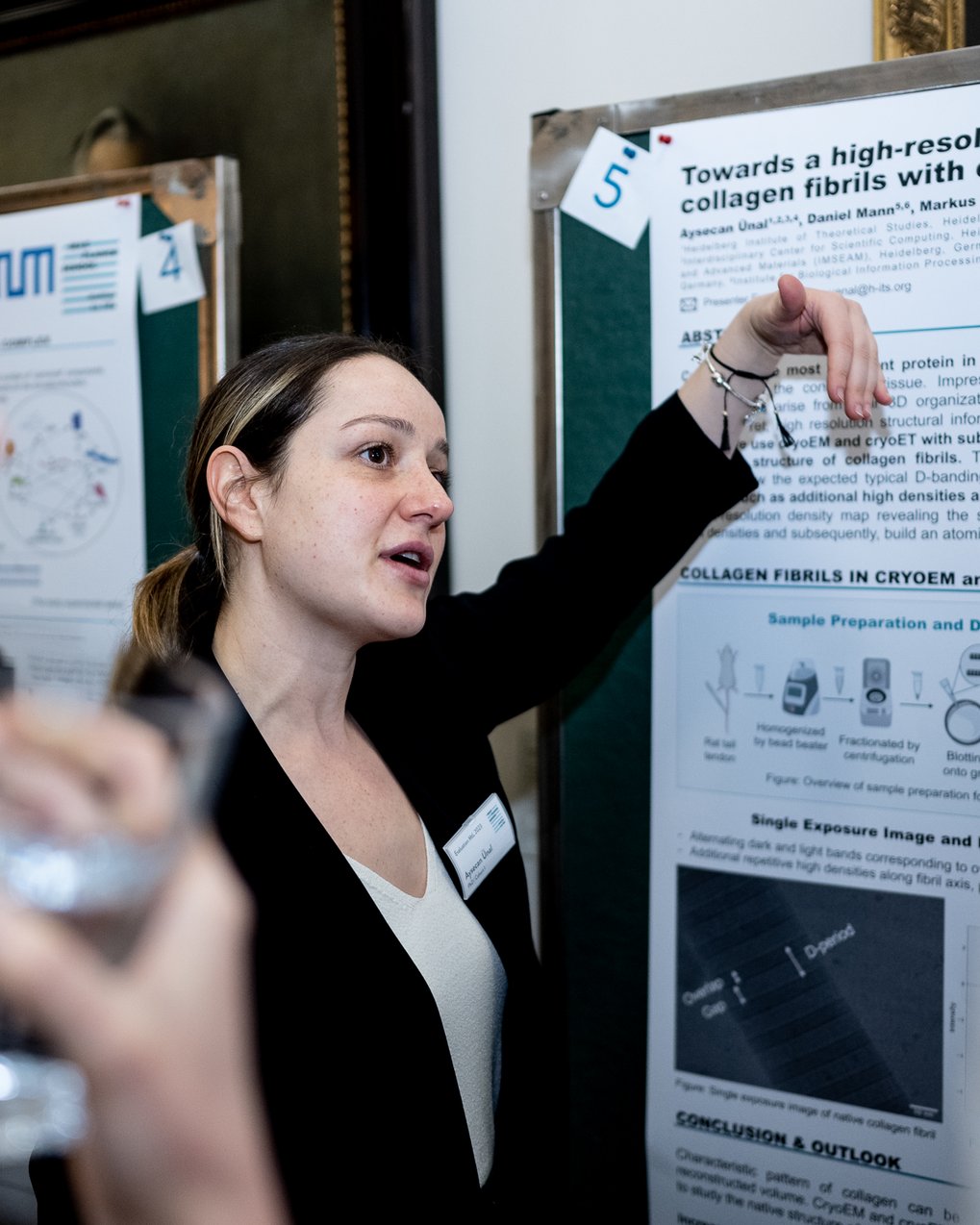 Aysecanpresents  a scientific research poster, pointing to a section while explaining findings.