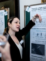 Aysecanpresents  a scientific research poster, pointing to a section while explaining findings.