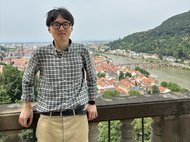 Won Joon Kim standing on a brigde,the city of Heidelberg and it's river is visible in the background